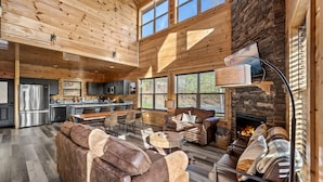 A spacious log cabin interior with a large living area, a fireplace, and a kitchen. - Luxurious 3BD Lodge with POOL! Hot Tub + Games! (Sevierville)