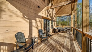 A wooden deck with Adirondack chairs and a table, overlooking a forested area. - Luxurious 3BD Lodge with POOL! Hot Tub + Games! (Sevierville)