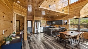 A spacious kitchen with wooden walls, a central island, and a dining area with chairs. - Luxurious 3BD Lodge with POOL! Hot Tub + Games! (Sevierville)