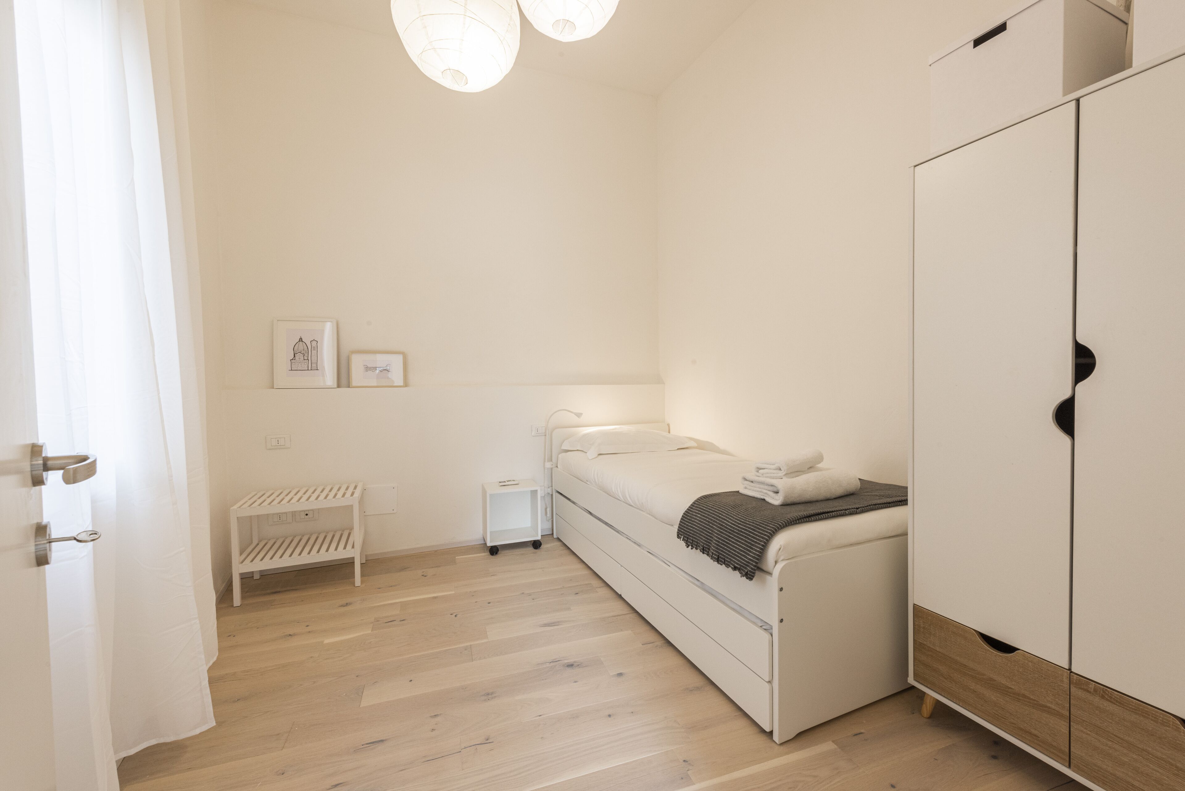 A bedroom with a bed, a wardrobe, a small bedside table, and a wall-mounted shelf.