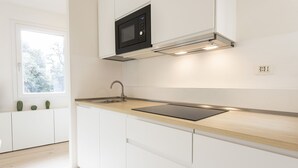 A modern kitchen with white cabinetry, a black microwave, a wooden countertop, and a window with a view of trees. - Torrigiani View by Mmega (Florence)