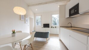 A modern kitchen with white cabinets, a black microwave, and a wooden countertop. There is a dining area with a white table and chairs, and a blue bench. - Torrigiani View by Mmega (Florence)