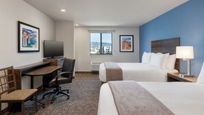 A hotel room with a bed, a desk with a chair, a television, and a window with a city view.