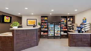 A reception area with a wooden reception desk, a refrigerator stocked with beverages, and shelves with snacks and toiletries.