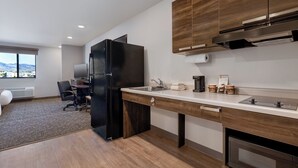 A modern kitchen with a black refrigerator, wooden cabinets, a stainless steel sink, and a window with a city view.