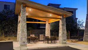 An outdoor patio with stone pillars, a covered seating area, and a grill.