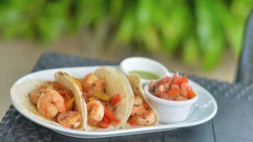 A plate of shrimp tacos with a side of salsa on a table with a green leafy background.
