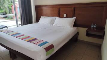 A neatly made bed with a colorful blanket, a wooden headboard, and a small nightstand with water bottles.