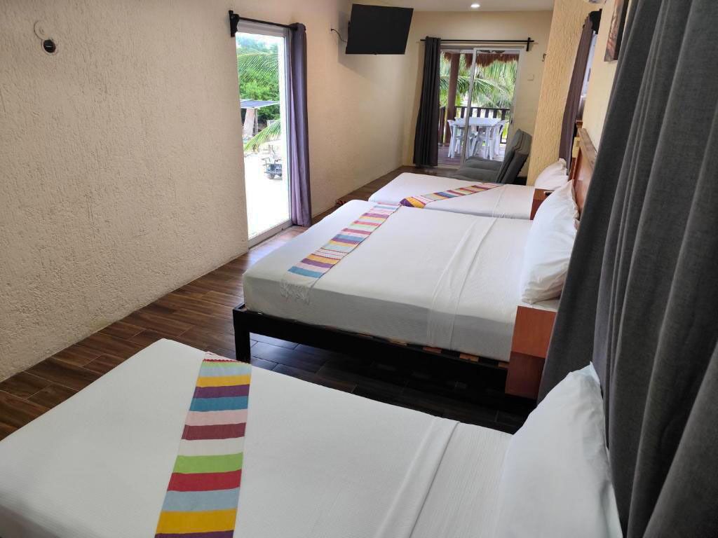 A hotel room with two beds, a television on the wall, and a balcony with outdoor seating.