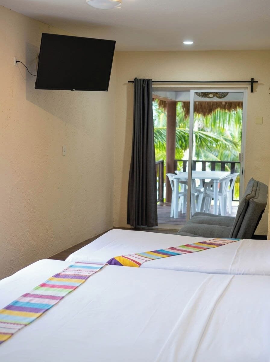 A hotel room with a bed, a TV mounted on the wall, and a balcony with a table and chairs.