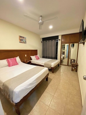 A hotel room with two beds, a ceiling fan, a painting on the wall, and a mirror.
