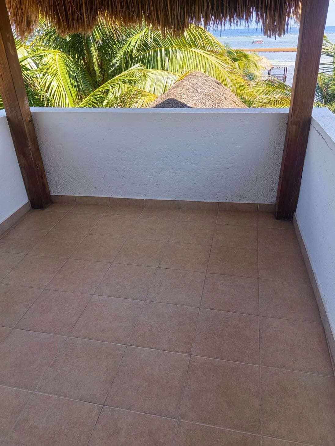 Een balkon met een betegelde vloer, een witte muur en een rieten dak.