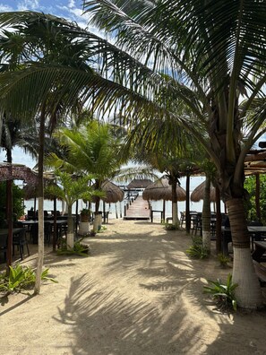 A beachside restaurant with thatched umbrellas, palm trees, and a wooden deck leading to the water. - 7mo Color Hotel Boutique (Mahahual)