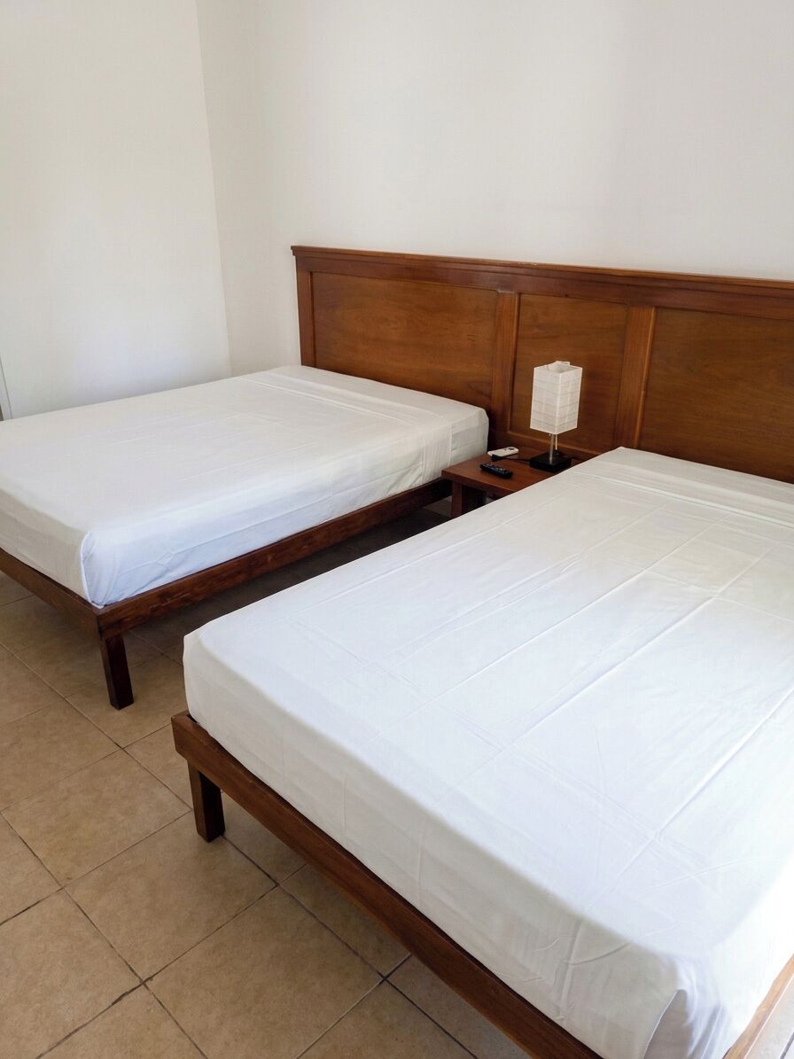 Twee enkele bedden met houten hoofdborden in een kamer met betegelde vloer.