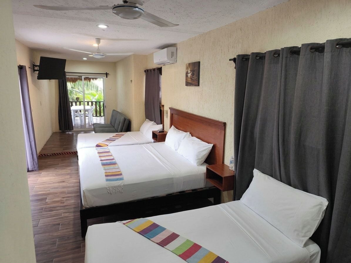 Habitación de hotel con dos camas, ventilador de techo, televisor de pantalla plana y vistas al exterior.