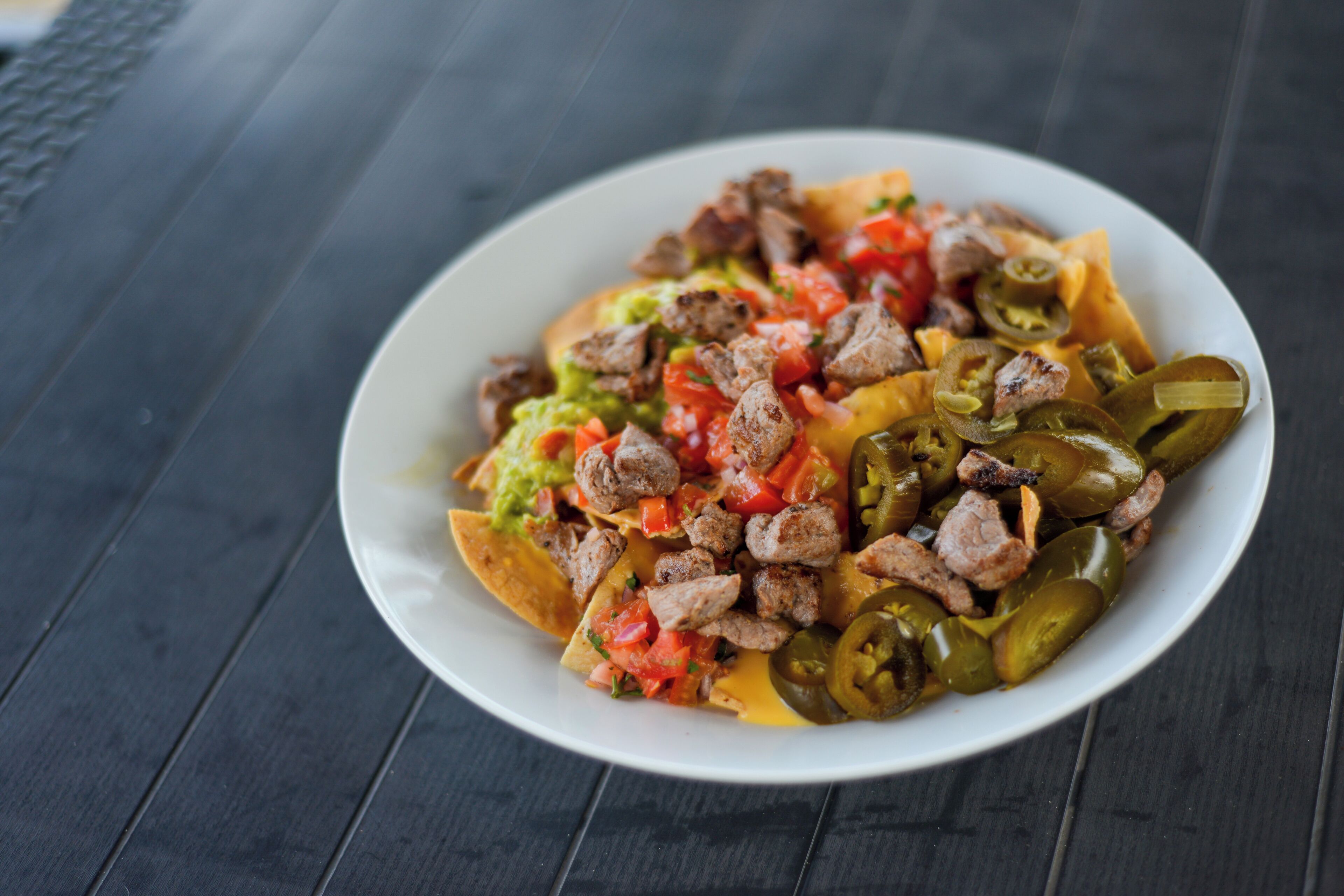 Un plato de nachos con carne, queso y jalapeños.