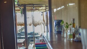 A bar area with a wooden counter, hanging decorations, and a view of the outdoor seating area. - 7mo Color Hotel Boutique (Mahahual)