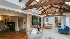 Un vaste espace de vie comprenant un piano, un canapé bleu et une structure de plafond en bois.