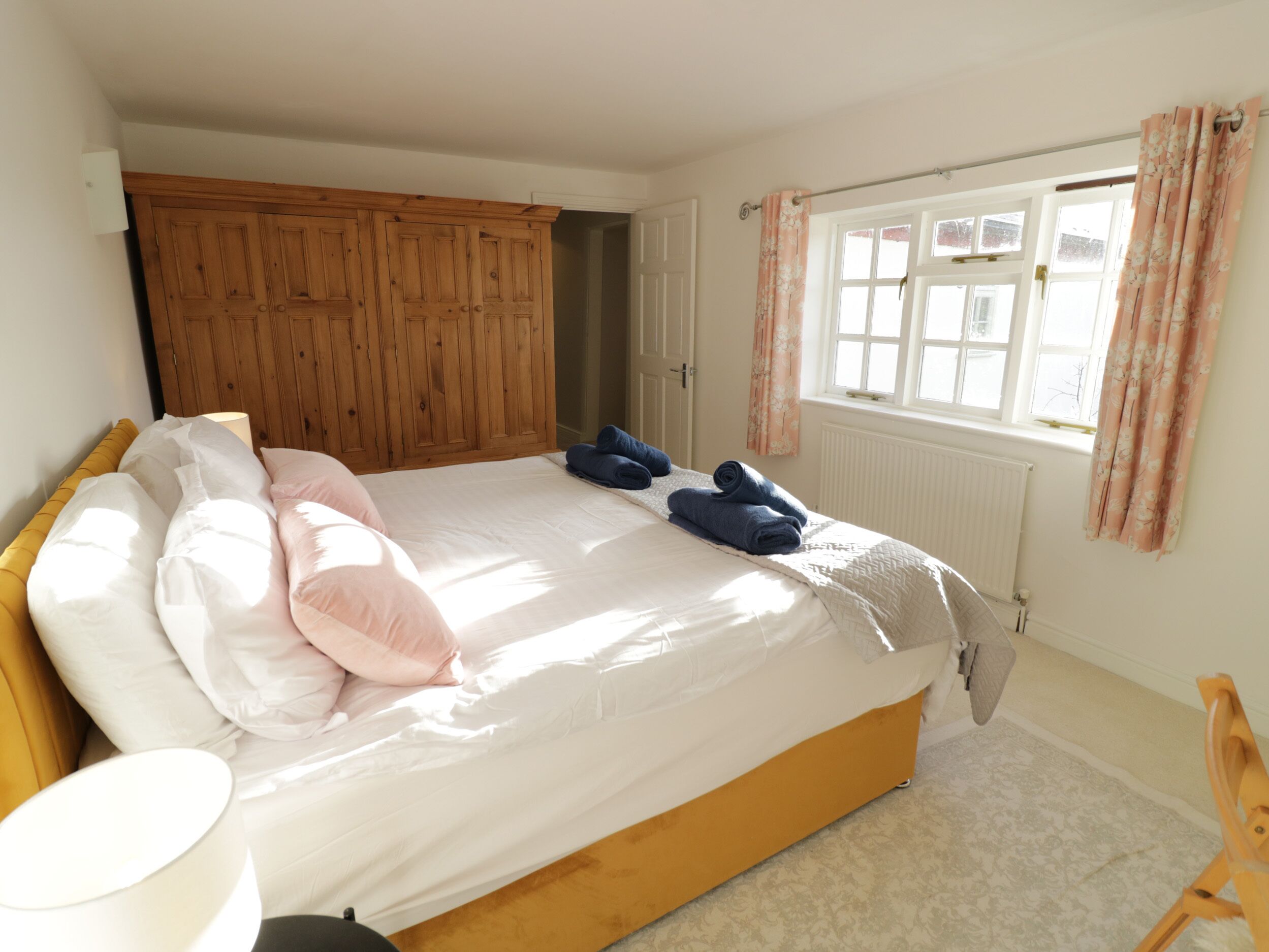Quarto com estrutura de cama de madeira, roupa de cama branca e janela com cortinas.