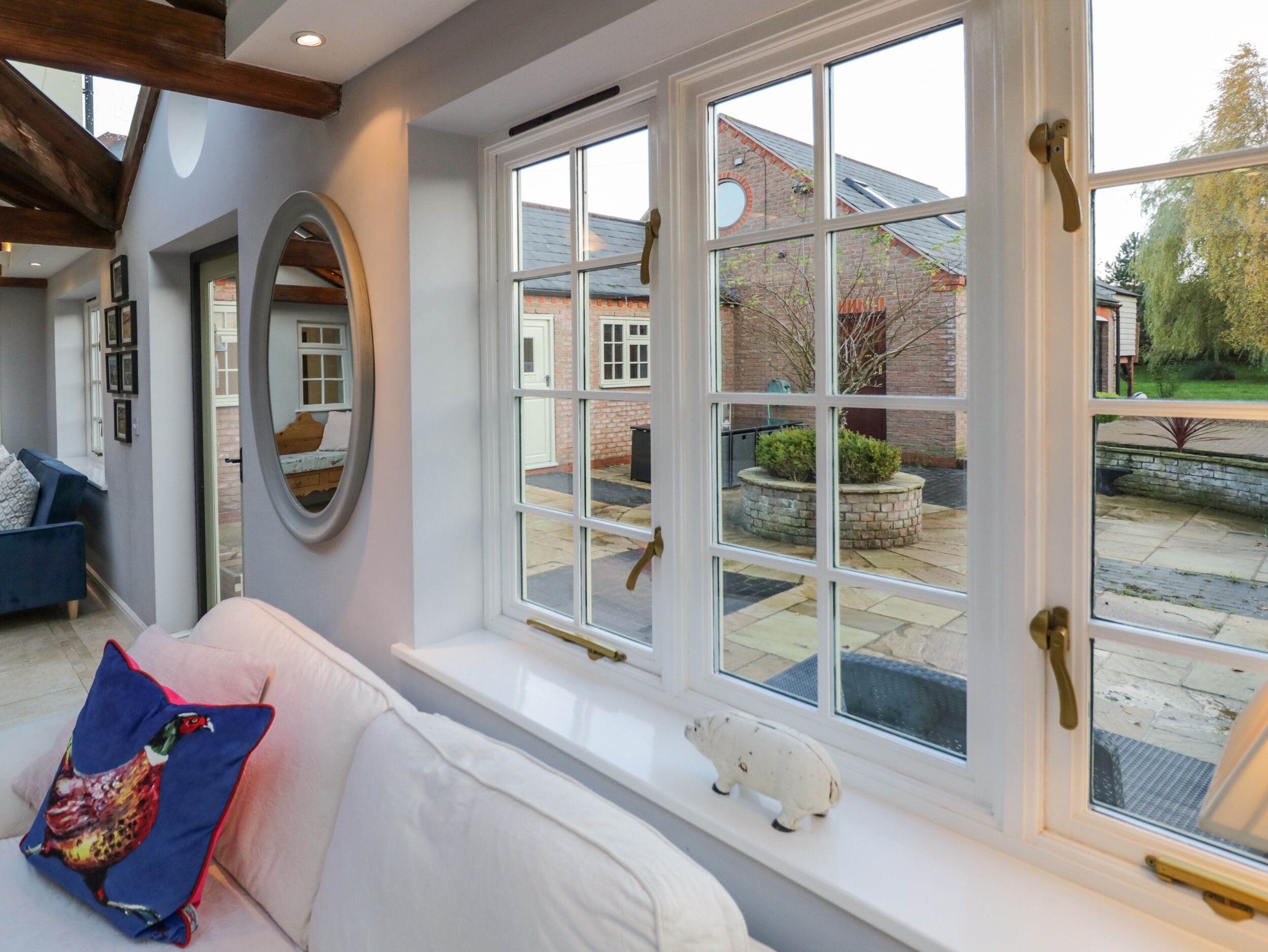 A room with a white sofa, a large window with multiple panes, a small white figurine on the windowsill, and a mirror on the wall.