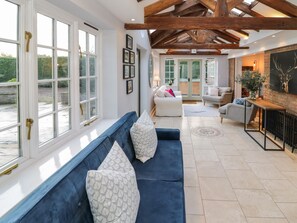 A spacious living room with a blue sofa, a fireplace, and a view of the outdoors. - Home Farm Cottage (Southam)
