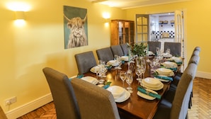 Une salle à manger avec une table en bois dressée pour six personnes, entourée de chaises recouvertes d’un tissu gris.