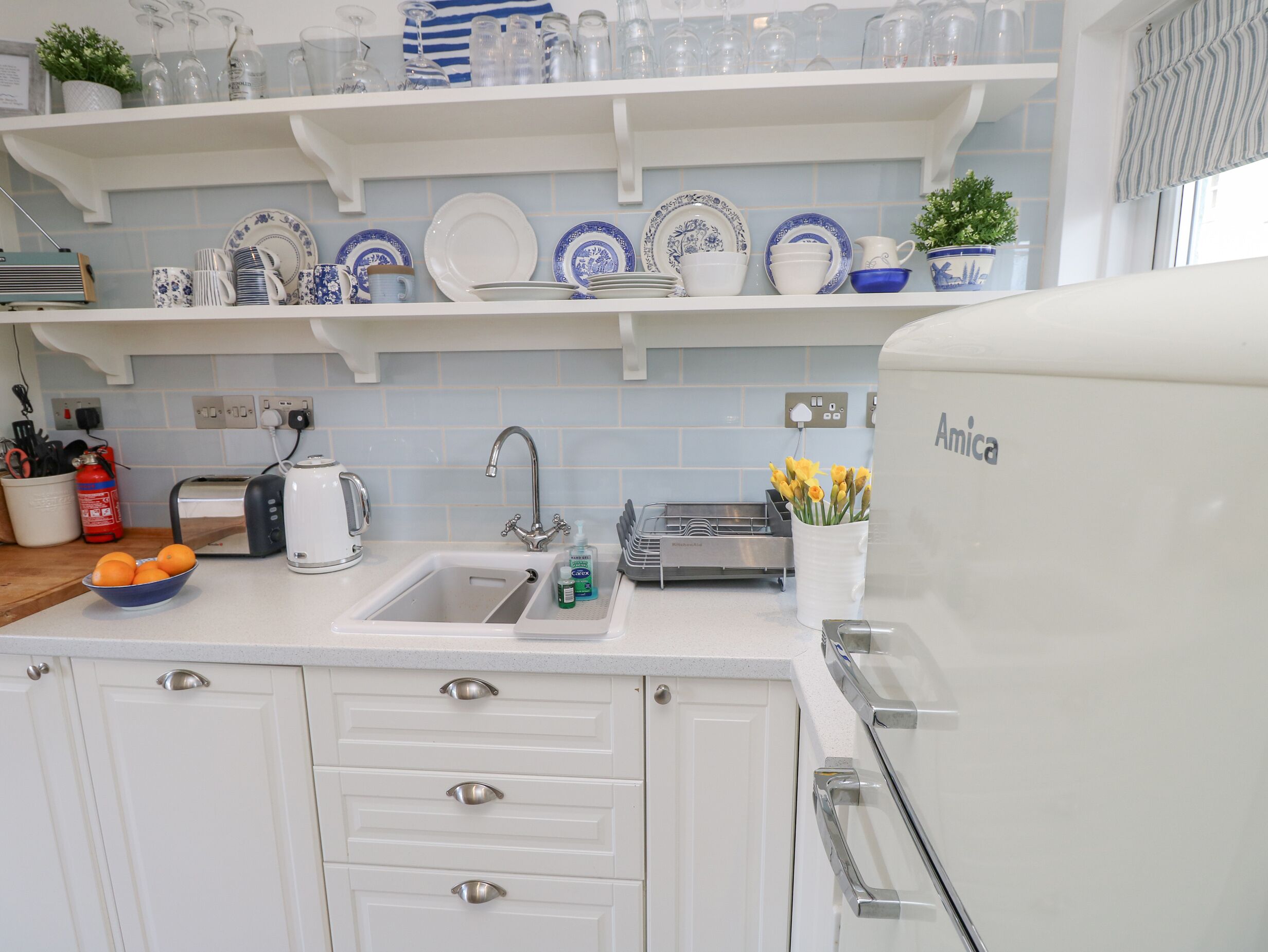 Una cocina con gabinetes blancos, un lavamanos, un tostador y un refrigerador.