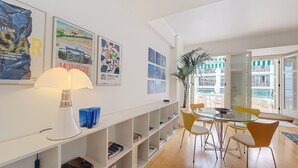 Ein modernes Wohnzimmer mit Essbereich, ausgestattet mit einer Bücherwand, einer Lampe und einem großen Fenster mit Blick ins Freie.