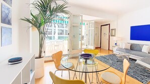 Ein modernes Wohnzimmer mit einem Glastisch, farbenfrohen Stühlen, einer großen Topfpflanze und einer Sofagarnitur.