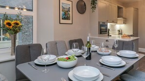 A dining area with a table set for four, a vase of sunflowers, a clock, and a framed picture on the wall. - Quarters (Ambleside)