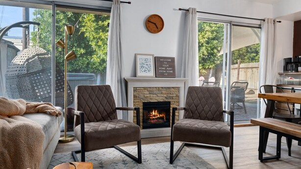 A modern living room with a fireplace, two armchairs, a sofa, and a dining area.