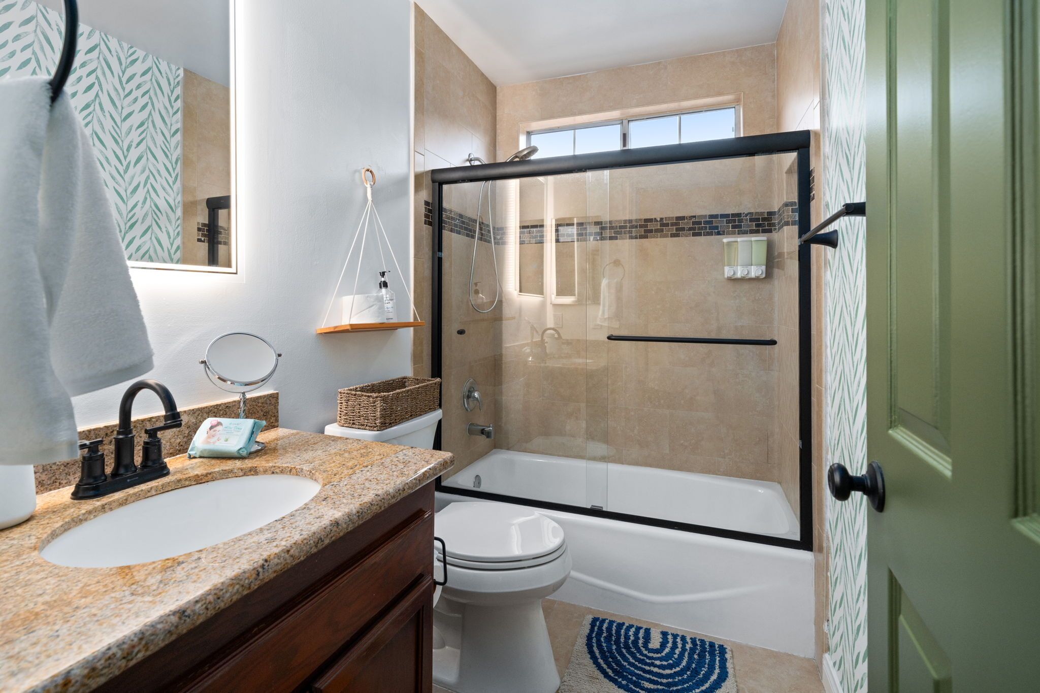 Une salle de bain avec un lavabo sur un plan de travail en granit, des toilettes, une douche à parois de verre et une porte verte.