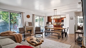 A modern living room with a fireplace, a dining area with a wooden table, and a kitchen with wooden cabinets and stainless steel appliances.