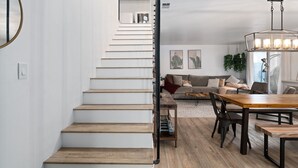 A staircase leading to a living area with a dining table and chairs, a sofa, and a hanging light fixture.