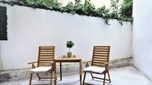 Two wooden chairs with cushions, a small table, and a potted plant in a corner with a white wall and greenery. - Unique Lodging (Athens)