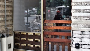 A building entrance with a large glass door, a wooden bench outside, and a stone wall with a number sign. - Unique Lodging (Athens)