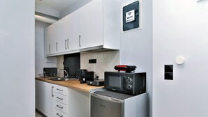 A compact kitchen with white cabinets, a stainless steel refrigerator, a microwave, and a coffee maker. - Unique Lodging (Athens)