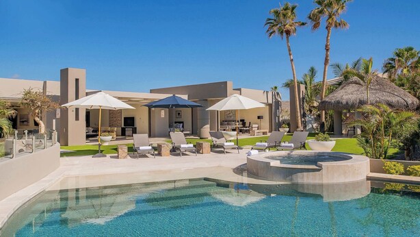 A pool area with lounge chairs and umbrellas, a clear pool, and a building with a modern design.