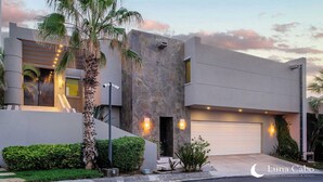 A modern building with a stone facade, a garage, and a well-maintained garden with palm trees and shrubs.