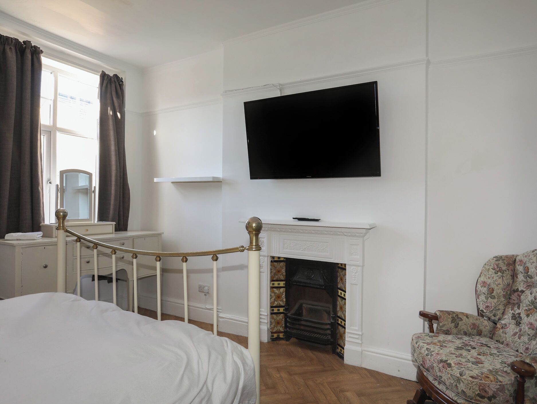 Una camera da letto con un letto, una televisione sopra un camino, una poltrona e una finestra con tende.