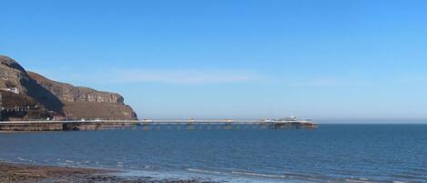 A coastal scene with a rocky beach, a pier extending into the sea, and a cliff in the background.