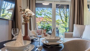 Een eettafel gedekt met witte borden, kommen en bestek, een vaas met een plant en een wijnglas.