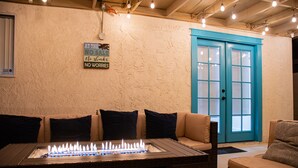 A cozy outdoor seating area with a fire feature, a sign with a humorous message, and a blue door. - Coachella Poolside Paradise, accommodates up to 10 guest (Indio)
