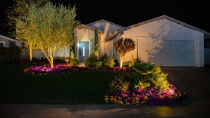 A residential house with a garage, well-maintained lawn, and colorful flower beds. - Coachella Poolside Paradise, accommodates up to 10 guest (Indio)