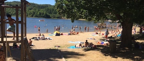Ein Strand mit einer Holzkonstruktion, entspannenden Menschen und einem See im Hintergrund.