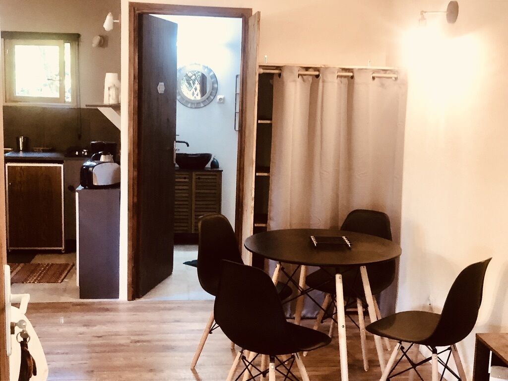 En matplats med ett runt bord och fyra stolar, ett kök som syns genom en öppen dörr och ett fönster med persienner.