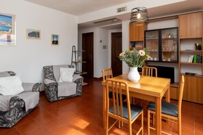 A living room with a wooden dining table, two patterned sofas, a TV cabinet, and a potted plant. - Casa di Titti by Wonderful Italy (Olbia)