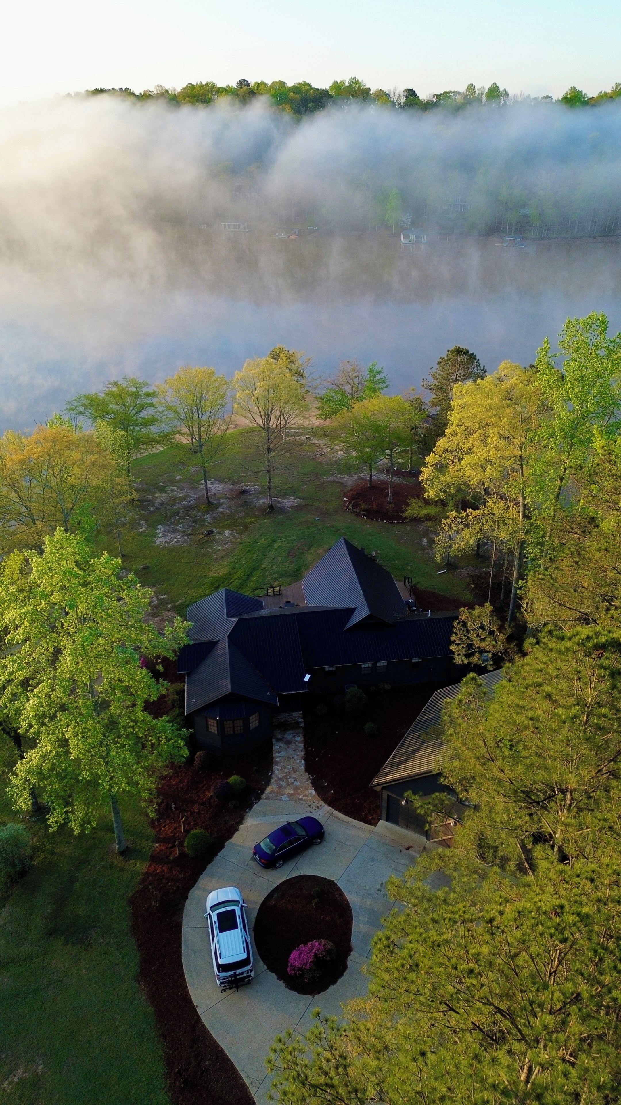 A house surrounded by trees and a lake, with a car parked in the driveway.