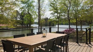 Un espace extérieur aménagé pour les repas, avec une table et des chaises en bois, donnant sur un lac bordé d’arbres et sur un quai.