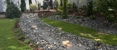 Un jardín ajardinado con un sendero de grava, césped y varios arbustos.